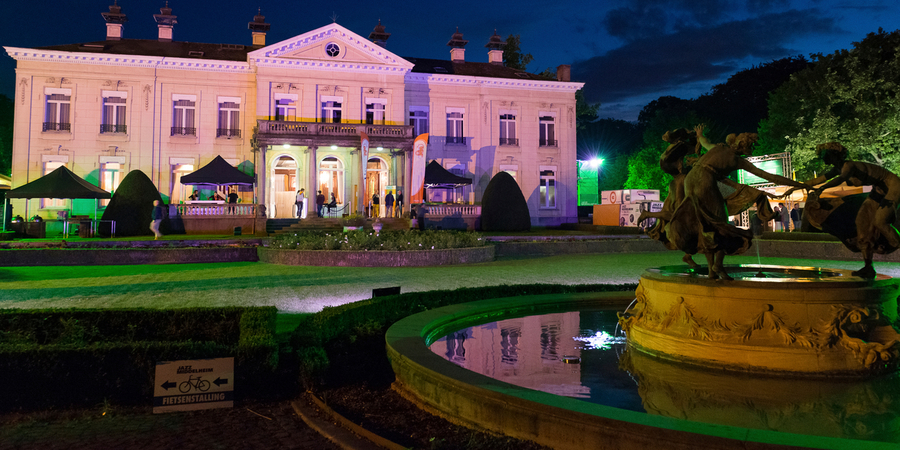 Het kasteel Den Brandt baadt in een roze schijn. Enkele mensen staan voor de ingang.